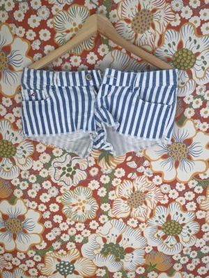 Blåvitrandiga shorts från Hollister - Säljer ett par blåvitrandiga shorts från Hollister med klassisk femficksdesign och rå kant nertill. Shortsen har låg midja och är gjorda i mjuk bomull, perfekta för varma dagar. Snyggt Hollister-märke bak i linningen.