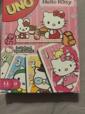 UNO Hello Kitty kortspel - UNO Hello Kitty kortspel med färgglada kort och motiv av Hello Kitty och hennes vänner. Lådan är rosa med vita rosor och innehåller en specialregel. Passar 2-10 spelare från 7 år. Perfekt för spelkvällar med vänner eller familj.