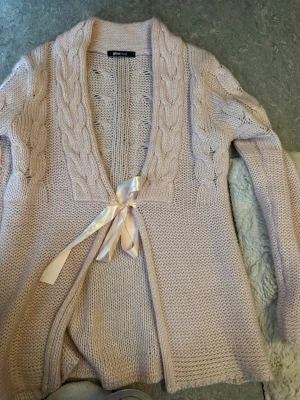 Ljusrosa stickad kofta med rosett - Supersöt ljusrosa stickad kofta som knyts med en sidenliknande rosett i midjan. 