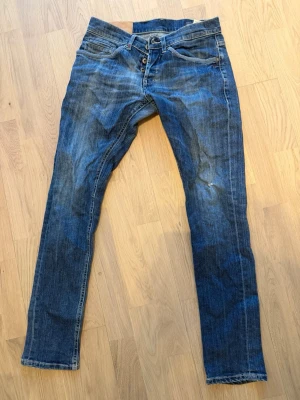 Blå smala jeans med knappgylf - Säljer ett par klassiska blå jeans med snyggt lagade framfickor med smal passform och knappgylf. Jeansen har fem fickor, slitningar och kontrastsömmar. Materialet är denim i bomull och de har en cool, något tvättad look. Perfekta till en avslappnad stil.