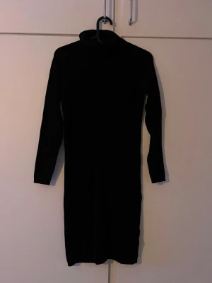 Svart stickad poloklänning - Säljer en svart stickad klänning med polokrage och lång ärm. Klänningen är enkel och stilren med en kroppsnära passform och når ungefär till knäna. Perfekt för dig som gillar en klassisk look med en mysig twist.