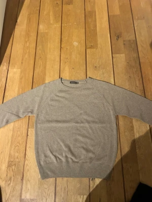 Beige stickad tröja med rund hals - En stilren beige stickad tröja med rund halsringning och långa ärmar. Tröjan har ribbade muddar vid ärmslut och nederkant. Perfekt för lager på lager och enkel att matcha med olika outfits.