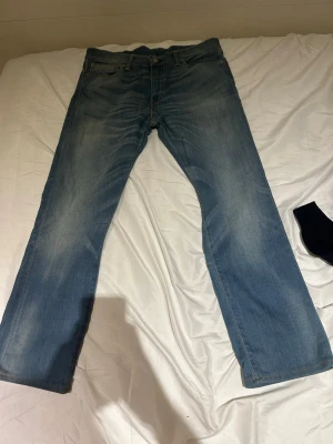 Ljusblå bootcutjeans från Levi's - Säljer ett par klassiska ljusblå jeans från Levi's med bootcut passform och fem fickor. Jeansen har slitningar och en vintagekänsla, perfekta för en avslappnad stil. Tillverkade i bomull med Levi's ikoniska läderpatch bak i midjan.