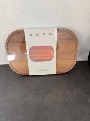 Smeg skärbräda i trä - Säljer en snygg och stilren skärbräda från Smeg i trä. Skärbrädan har en rektangulär form med rundade hörn och en naturlig träfärg. Perfekt för köket när du vill ha både funktion och design.