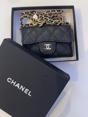 Svart Chanel quiltad miniväska - Supersnygg svart miniväska från Chanel i quiltat läder med guldfärgade detaljer och kedjerem. 
