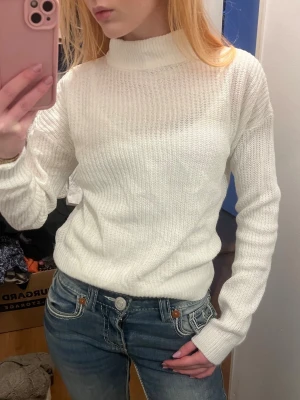 Vit ribbstickad polotröja - Säljer en enkel och stilren vit ribbstickad tröja med hög krage och långa ärmar. Tröjan har en klassisk passform och är perfekt att matcha med jeans eller kjol. Materialet känns mjukt och bekvämt mot huden.