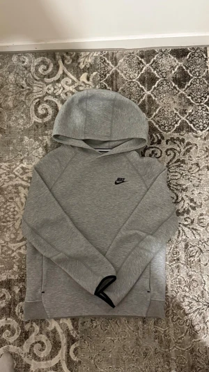 Grå hoodie från Nike med huva - Snygg grå hoodie från Nike med klassisk logga broderad på bröstet. Hoodien har en mjuk och bekväm känsla, huva och långa ärmar. Perfekt för en avslappnad streetwear-look. Tillverkad i ett mjukt material som känns skönt mot huden.
