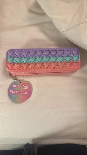 Pop It pennfodral i pastellfärger - Säljer ett Pop It pennfodral i silikon med hjärtformade bubblor. Fodralet har pastellfärger i lila, turkos och rosa och stängs med dragkedja. Perfekt för att förvara pennor och småprylar, och du kan poppa bubblorna när du vill slappna av.