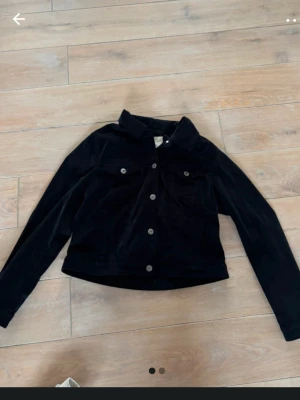 Svart mockajacka från Esprit - Stilren svart mockajacka från Esprit med klassisk krage, två bröstfickor med lock och silverfärgade knappar framtill. Jackan har en rak passform och långa ärmar, perfekt för en trendig och avslappnad look.