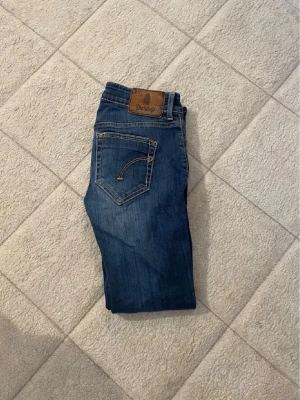 Blå jeans från Dondup - Säljer ett par klassiska blå jeans från Dondup med snygga kontrastsömmar och detaljerade bakfickor. Jeansen har en normal passform och är tillverkade i slitstark denim. Perfekta för dig som gillar en tidlös och stilren look.