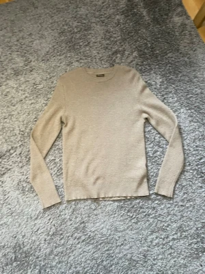 Stenstöms Beige stickad tröja med rund hals - En stilren beige stickad tröja med rund halsringning och långa ärmar. Tröjan har en diskret struktur i stickningen och ribbade muddar vid ärmslut och nederkant. Perfekt för lager på lager och enkel att matcha med olika outfits.