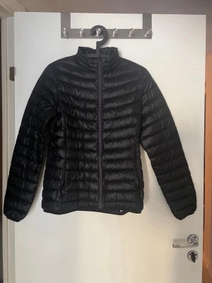 Svart lättviktsjacka från Everest - Snygg svart lättviktsjacka från Everest med quiltad design och hög krage. Jackan har dragkedja framtill och är lätt vadderad,. Enkel och stilren modell som passar till det mesta. Storlek 38.