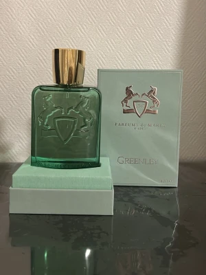 Parfums de Marly Greenley EdP 125ml - Greenley från Parfums de Marly är en exklusiv parfym i en elegant grön glasflaska med guldfärgat lock. Flaskan har ett stilrent emblem med två hästar och sköld. Kommer i originalkartong i matchande grön nyans. Lyxig och modern doft för dig som gillar unika parfymer.