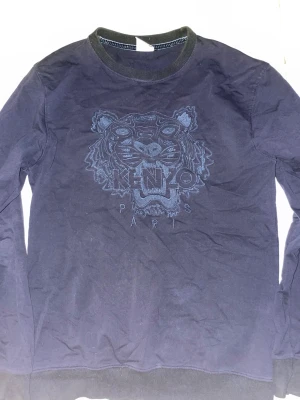 Mörkblå Kenzo sweatshirt med tiger - Snygg svart sweatshirt från Kenzo med det ikoniska tigerhuvudet broderat framtill och texten 'Kenzo Paris'. Tröjan har rund halsringning och ribbade muddar. Perfekt för dig som gillar streetwear och vill ha något trendigt i garderoben.