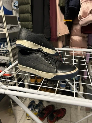 Lanvin captoe - Snygga svarta sneakers från Lanvin med crocopräglat mönster och vita/blåa sulor. Skorna har svarta skosnören och en klassisk låg profil. Materialet ser ut att vara konstläder med struktur för en cool look. De är storlek 41 men passar mer 42 ungefär.
