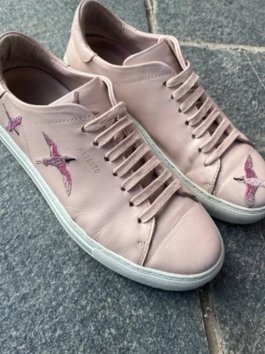 Ljusrosa sneakers från Axel Arigato - Snygga ljusrosa sneakers från Axel Arigato i skinn med broderade fåglar i rosa och lila på sidan och tån, perfekta till vår och sommar! Klassisk låg modell med ljusrosa snörning. Lätt slitage som man ser på bilderna. Storlek 40, man får med originalpåsen som syns på sista bilden. Nypris ca 3000💗
