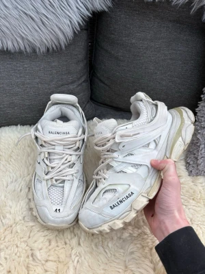 Balenciaga Track vita sneakers - Chunky vita Balenciaga Track sneakers med mesh och syntetpaneler, kraftig sula och logga på sidan och plös. Skorna har en futuristisk design med flera lager och detaljerade snörningar. Perfekta för dig som gillar statement-sneakers.
