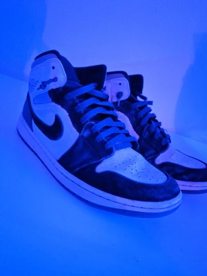 Nike Air Jordan 1 svart/vit high - Säljer ett par Nike Air Jordan 1 high sneakers i svart och vitt med klassisk Swoosh på sidan. Skorna har högt skaft, perforerad tåbox och signaturdetaljer vid ankeln. Perfekta för dig som gillar streetwear och ikonisk design.