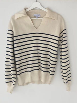 Randig stickad tröja med krage - Snygg stickad tröja i offwhite med mörkblå horisontella ränder. Tröjan har en bred krage och v-ringning, samt långa ärmar med ribbade muddar. Perfekt för en avslappnad men stilren look. Materialet känns mjukt och bekvämt.