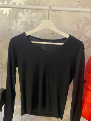 Svart ribbad långärmad topp - En svart, ribbad långärmad topp med v-ringning. Enkel och stilren design som passar till det mesta. Tillverkad i ett mjukt och stretchigt material för en bekväm passform.