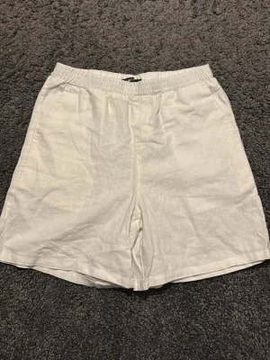 Vita linneshorts från lmtd - Snygga och luftiga vita shorts i linne med elastisk midja för skön passform. Perfekta för varma dagar och enkel att matcha med olika stilar. Klassisk design utan synliga detaljer eller mönster.