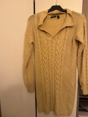 Beige kabelstickad tröja Brave Soul - Beige kabelstickad tröja från Brave Soul med v-ringning och krage. Långärmad modell med breda flätmönster framtill och ribbade muddar. Perfekt för dig som gillar en avslappnad men ändå snygg stil.