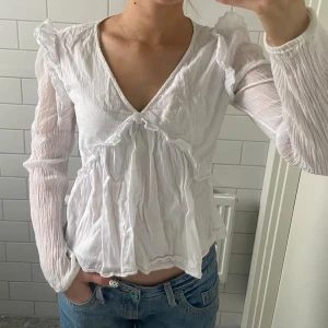 Vit volangblus med v-ringning - Söt vit blus med v-ringning och volangdetaljer, lite rynkat tyg på ärmarna. Från Gina Young, egentligen storlek 170 men sitter som en XS/S skulle jag säga! Finns vissa svaga missfärgningar men det syns knappt 😊