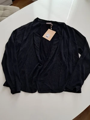 Svart öppen kofta från Kaffe - Stilren svart öppen kofta från Kaffe med lång ärm och mjukt, tunt material. Perfekt att slänga över en topp för en avslappnad look. Enkel design utan knappar eller dragkedja.