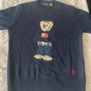 Mörkblå stickad tröja Polo Bear RL - Mörkblå stickad tröja från Polo Ralph Lauren med ikoniska Polo Bear-motivet framtill. Tröjan har rund hals, ribbade muddar och RL-broderi i rött nedtill. Materialet är mjukt och passar perfekt för en cool och avslappnad stil. Hör av er vid funderingar! PRIS KAN DISKUTERAS VID SNABB AFFÄR! 
