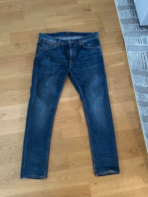 Blå jeans från Nudie Jeans - Snygga blå Nudie Jeans med klassisk femficksmodell och raka ben. Jeansen har orangea kontrastsömmar och är tillverkade i slitstark denim. Perfekta för dig som gillar en tidlös och enkel stil samt trendig.