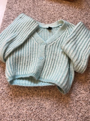 Ljusblå stickad kofta med knappar - Superfin ljusblå stickad kofta med v-ringning och tre knappar framtill. Koftan är kortare i modellen och har breda, ribbstickade ärmar. Mjuk och fluffig känsla, perfekt för lager-på-lager. Passar dig som gillar en chill och trendig stil. Kan tas bort om jag ångrar mig!