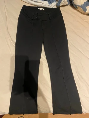 Svarta kostymbyxor med utsvängda ben - Snygga svarta kostymbyxor med utsvängda ben och låg midja i storlek 158. Byxorna har två knappar framtill och markerad pressveck längs benen. Perfekta för en stilren och trendig look. Säljer då de tyvärr är för korta för mig, har någon dessa byxor i 164 får ni gärna skriva till mig💕 