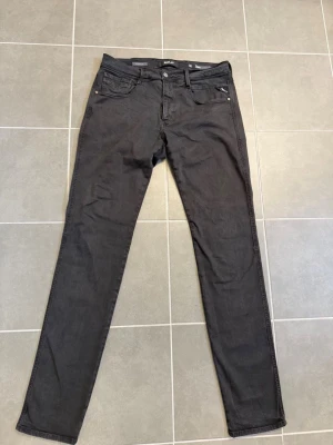 Svarta slim fit jeans från Replay W32 L34 - Snygga svarta slim fit jeans från Replay med klassisk femficksdesign och silverfärgade nitar. Jeansen har normal midja och raka ben. Materialet är mjukt och stretchigt för extra komfort. Perfekta för en trendig och avslappnad stil.