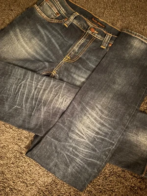 Nudie Jeans Tube Kelly Slim Fit Dark Indigo - Nudie Jeans Tube Kelly i perfekt ingången Dark Indigo med väldigt snygga fades/slitningar. Ett par riktigt snygga jeans som inte tillverkas längre. Premiumkänsla med djup indigoblå tvätt och stark karaktär. 🧵 Märke & Modell: Nudie Jeans Co - Tube Kelly. 📏 Storlek & Passform: W30 L32, slim fit med normal midja och skön stretch. 🧩 Material: 99% bomull, 1% elastan. 📐 Mått: A 40 cm B 78 cm C 102 cm. ✅ Skick: 9/10, mycket fint skick. Använda lite. 🕺 Passar ca 175-180 cm. ‼️Skickar samma dag ‼️