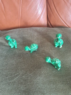 Charmig kvartett av sköldpaddor i glaserad keramik! - Säljer fyra stycken små sköldpaddsfigurer i en härlig grön nyans med fin lyster. Sköldpaddorna har olika poser och uttrycksfulla ansikten, vilket gör dem till ett perfekt tillskott i samlarhyllan eller som en lekfull detalj i inredningen. Antal: 4 stycken. Material: Glaserad keramik/porslin. Färg: Gräsgrön med mörkare detaljer i skalet. 