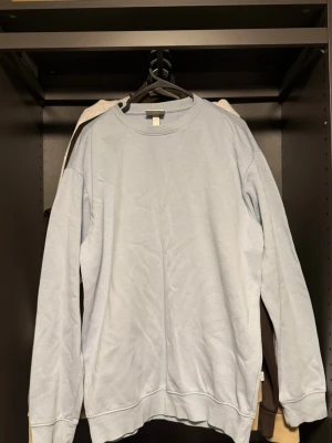 Ljusblå basic sweatshirt - En enkel ljusblå sweatshirt med rund hals och ribbade muddar vid ärmslut och nederkant. Tröjan har en avslappnad passform och är tillverkad i mjukt material, perfekt för en casual look.