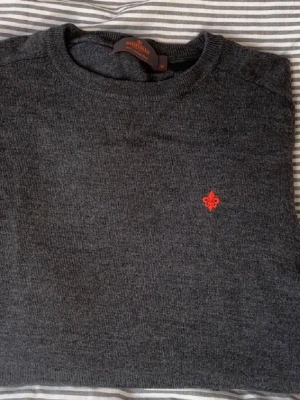 Mörkgrå stickad tröja Morris M - Snygg mörkgrå stickad tröja från Morris i 100% merinoull. Tröjan har rund halsringning och en liten röd broderad logga på bröstet. Perfekt för dig som gillar klassisk och stilren design. Pris kan diskuteras vid snabb affär 