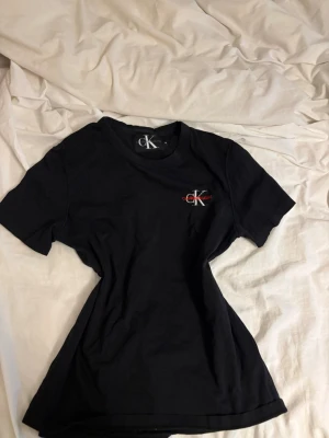 Svart Calvin Klein t-shirt - Snygg svart t-shirt från Calvin Klein med liten CK-logo broderad på bröstet i vitt och rött. Klassisk rund hals och korta ärmar. Perfekt basplagg med stilren design och skön passform i mjuk bomull.