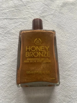 Honey Bronze Shimmering Dry Oil - The Body Shop Honey Bronze Shimmering Dry Oil är en torr olja som ger huden en solkysst lyster. Den har en lätt konsistens som snabbt absorberas av huden. Oljan ger en subtil skimmereffekt och passar för alla hudtyper. Volym: lite mindre än 100 ml, se pilen. 