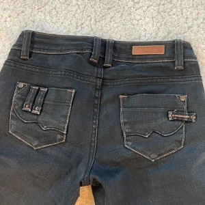 Svarta bootcut jeans  - Säljer ett par svarta jeansbyxor med unika detaljer på bakfickorna. Säljer pågrund av att dom inte passar storlek eller längd då de va för långa.💕
