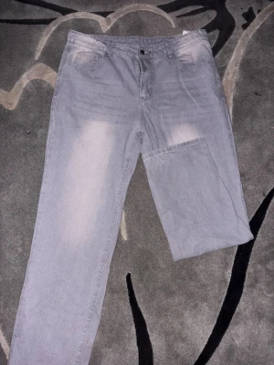 Grå jeans med blekta detaljer - Säljer ett par grå jeans med blekta partier på framsidan och baksidan. Klassisk femficksdesign och raka ben. Jeansen har knappstängning och är tillverkade i denim. Perfekt för dig som gillar en avslappnad och trendig look.