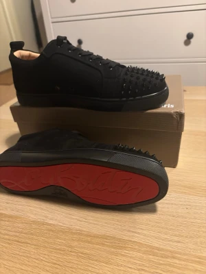 Svarta Louboutin sneakers med nitar - Säljer ett par svarta sneakers från Christian Louboutin som är i princip helt oanvända. Skorna har en låg profil, snörning och är tillverkade i mocka och läder.