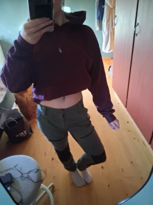 Gröna cargobyxor med svarta detaljer - Säljer ett par gröna cargobyxor med svarta paneler på knäna och praktiska fickor på sidorna. Byxorna har en modern, slim fit och är perfekta för dig som gillar en avslappnad och cool stil. Materialet ser ut att vara bomull eller en bomullsblandning. Den ena byx-drakedjan är trasig💕