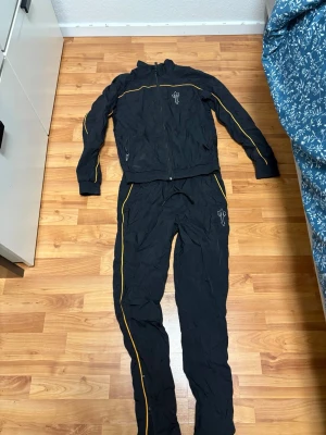 Trapststar Tracksuit - Säljer en svart tracksuit från Trapstar i storlek XS. Setet består av jacka med dragkedja och byxor med resår och dragsko. Båda delarna har gula detaljer längs sidorna och Trapstar-logga på bröst och lår. Perfekt för träning eller chill.