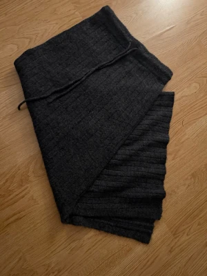 Mörkgrå stickad kjol - Mysig mörkgrå kjol i stickat material med diskret rutmönster och ribbade kanter. Perfekt för kalla dagar och enkel att matcha med olika outfits. Tjock och varm, passar dig som gillar stilrena accessoarer.