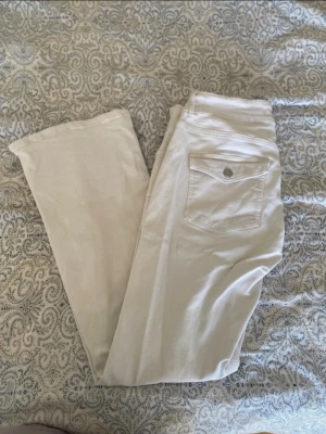 Vita jeans med fickdetalj - Snygga vita jeans med flared passform och en bakficka med knappdetalj. Jeansen har klassisk femficksdesign och är tillverkade i ett mjukt bomullsmaterial. Perfekta för en clean och fräsch look. Jeansen är från Nelly och är i storlek 44