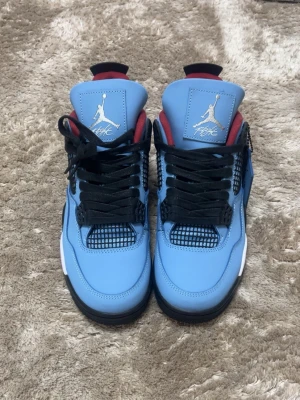 Jordan 4 Retro Travis Scott blå - Säljer ett par Jordan 4 Retro Travis Scott sneakers i ljusblå med svarta och röda detaljer   Helt nya med box och aldrig använda. Skorna har svart nät på sidorna, svarta skosnören och vit/svart sula med synlig Air-enhet. Insidan är röd och tungan har Jumpman-logga i vitt..