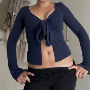 Mörkblå långärmad knytblus 💙 - Säljer en mörkblå långärmad blus med djup v-ringning och snygg knytning framtill. Toppen är croppad och har en figurnära passform med långa ärmar. Säljer den för jag har ingen användning till den! 💕
