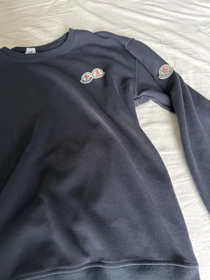 Svart sweatshirt från Moncler - Snygg mörkblå sweatshirt från Moncler med rund halsringning och ribbade muddar. Tröjan har Moncler-logga på bröstet och på ena ärmen. Jag är 175 cm lång och passar mig bra. Proset kan diskuteras.