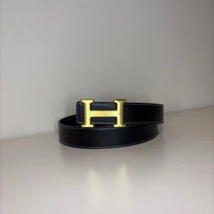 Svart skärp med gulddetalj - Snyggt svart skärp från  med ikoniskt H-spänne i guld. Skärpet har vita kontrastsömmar och är gjort i exklusivt skinn. Perfekt accessoar för att lyfta vilken outfit som helst.